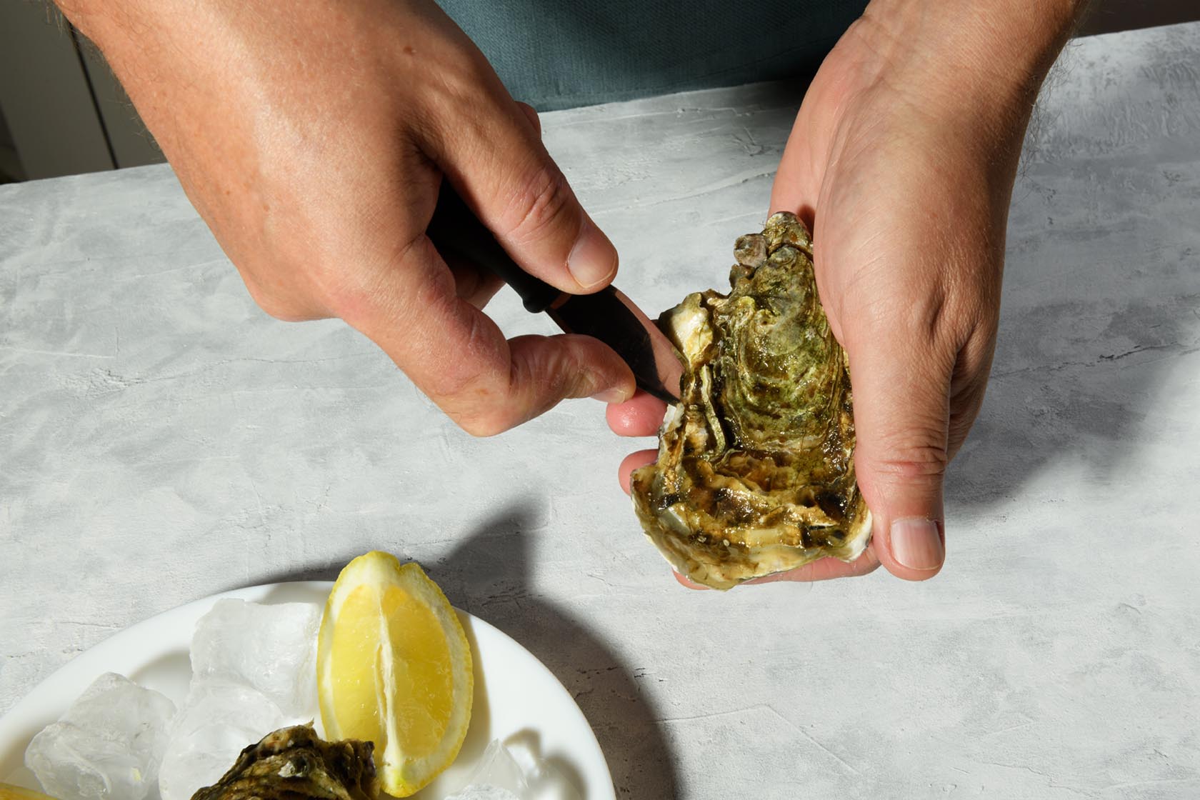 A man's hands are shucking fresh oysters with a blade of knife,
